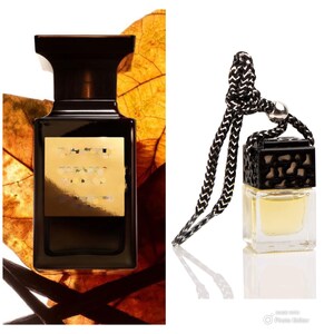 May include: A black and gold bottle of perfume with a black cap. The bottle is sitting on a brown leaf. A black and gold car air freshener with a black string is also shown.