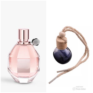 May include: A pink glass bottle of perfume with a rose gold cap and a clear glass atomizer. The bottle is shaped like a rounded octagon.  Next to the bottle is a small, round, blue glass bottle with a wooden cap and a brown rope.