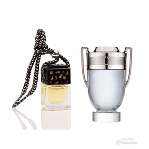 May include: A silver and black car air freshener with a black string for hanging. The air freshener is shaped like a bottle and has the word "INVICTUS" on the top. The air freshener is next to a smaller, clear bottle with a black cap and a black and gold patterned design.