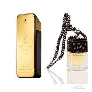 May include: A gold and black bottle of perfume with a matching car air freshener. The air freshener is hanging from a black cord.