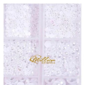 May include: A clear plastic container with four compartments filled with white pearl-like beads and sequins. The container has the text "Million Krystals" printed on the front.