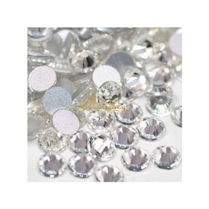 May include: A close-up of a large quantity of clear glass rhinestones. The rhinestones are scattered on a white surface.