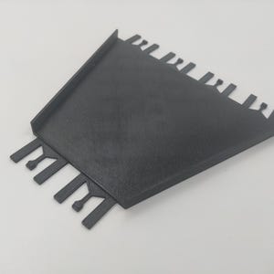 May include: Black plastic tool with a flat base and multiple teeth on the sides. The tool is designed for spreading mortar or grout.