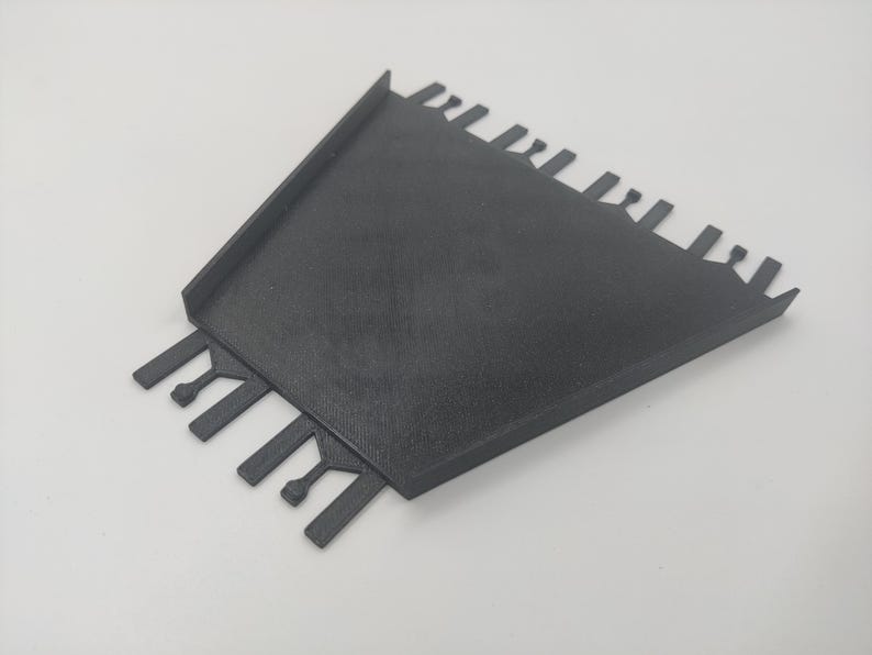 May include: Black plastic tool with a flat base and multiple teeth on the sides. The tool is designed for spreading mortar or grout.