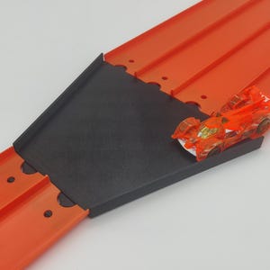 May include: A red and black Hot Wheels track set with a car on the track. The track is made of plastic and has a black ramp.