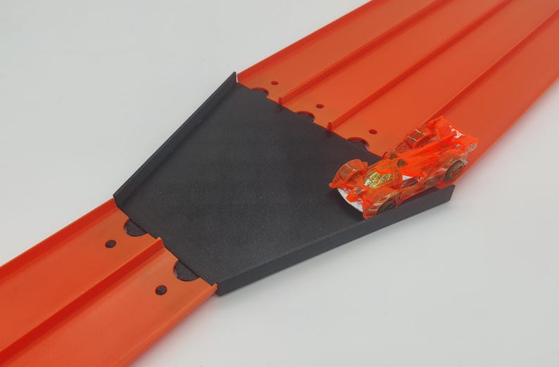 May include: A red and black Hot Wheels track set with a car on the track. The track is made of plastic and has a black ramp.