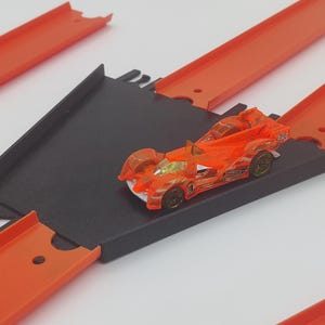 May include: A black and orange toy race car on a black and orange track set. The car is on a ramp and the track is made of plastic.