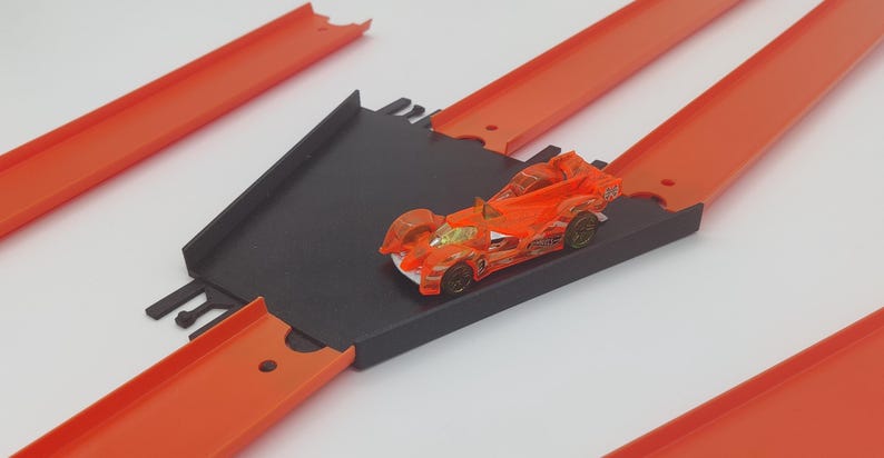 May include: A black and orange toy race car on a black and orange track set. The car is on a ramp and the track is made of plastic.
