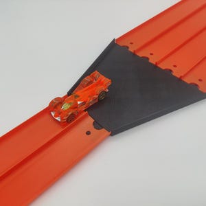 Op de afbeelding: Oranje speelgoed racebaan met een zwarte plastic helling en een kleine oranje speelgoedauto op de baan.