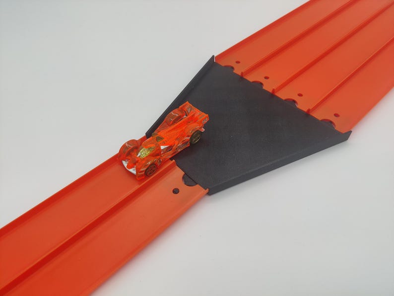 May include: Orange toy race car track with a black plastic ramp and a small orange toy car on the track.