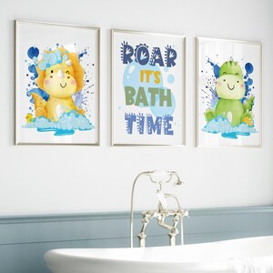 May include: Three framed prints with a blue, yellow, and green dinosaur theme. The center print says "Roar It's Bath Time" in blue and yellow letters. The prints are perfect for a child's bathroom.