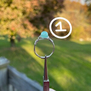 K&ouml;nnte beinhalten: Ein Ring aus Silberdraht mit einem hellblauen Edelstein. Der Ring befindet sich auf einem Pr&auml;sentationsst&auml;nder.