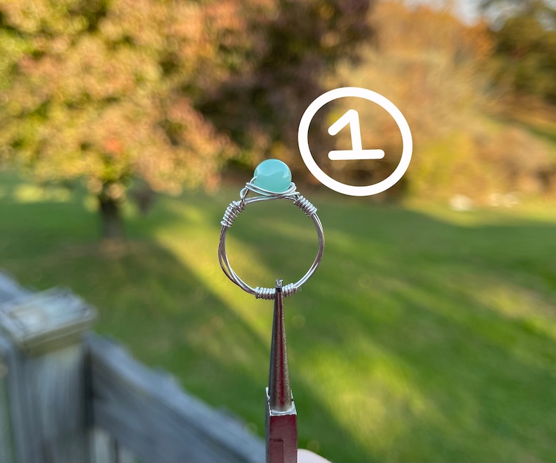 K&ouml;nnte beinhalten: Ein Ring aus Silberdraht mit einem hellblauen Edelstein. Der Ring befindet sich auf einem Pr&auml;sentationsst&auml;nder.