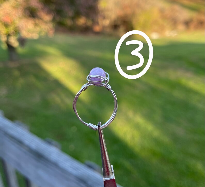 K&ouml;nnte beinhalten: Ein Ring aus silbernem Draht mit einem hellvioletten Edelstein. Der Ring wird von einer Zange gehalten.