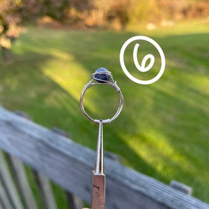 K&ouml;nnte beinhalten: Ein Ring aus Silberdraht mit einem blauen Edelstein. Der Ring wird von einer Zange gehalten.