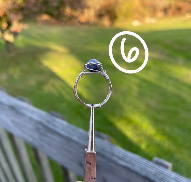 K&ouml;nnte beinhalten: Ein Ring aus Silberdraht mit einem blauen Edelstein. Der Ring wird von einer Zange gehalten.