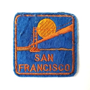 May include: A blue felt patch with orange embroidery depicting the Golden Gate Bridge and the words "SAN FRANCISCO".