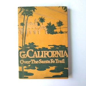 May include: A vintage book cover with a yellow background and green illustrations of palm trees and a building. The title of the book is "To California Over The Santa Fe Trail."