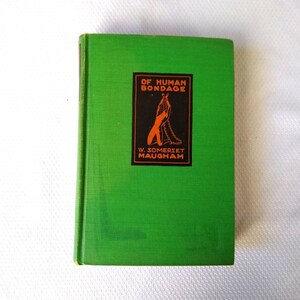 May include: A green hardcover book with the title "Of Human Bondage" and the author's name "W. Somerset Maugham" printed on the front cover.