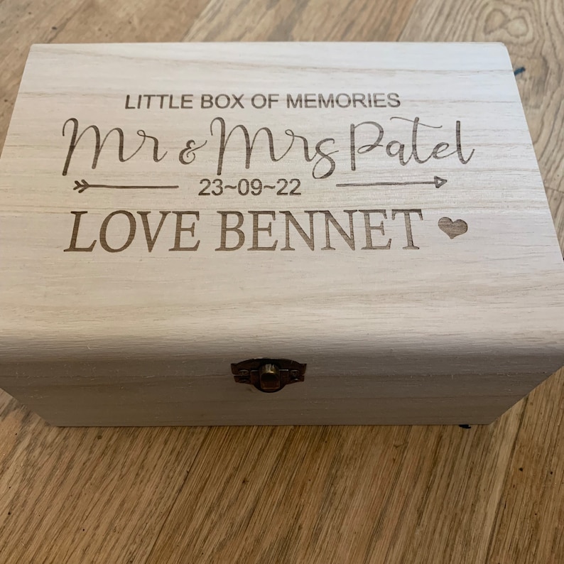 May include: A wooden box with a hinged lid and a brass latch. The box is engraved with the text "Little Box of Memories", "Mr & Mrs Patel", "23-09-22", "LOVE BENNET" and a heart.
