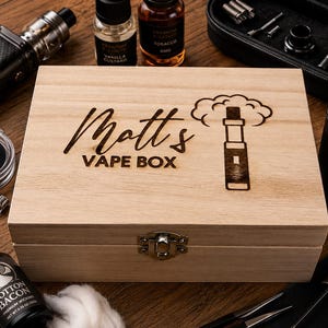 May include: A rectangular light-coloured wooden storage box with a silver metal latch. The lid is laser-engraved with the text "Matt's VAPE BOX" and a graphic of a vape pen emitting a cloud of vapour, surrounded by various vaping accessories.