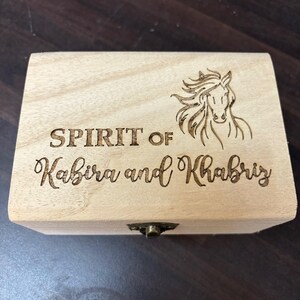 May include: A wooden box with a hinged lid and a brass latch. The box is engraved with the words "SPIRIT OF Kabira and Khabriz" and a horse's head.