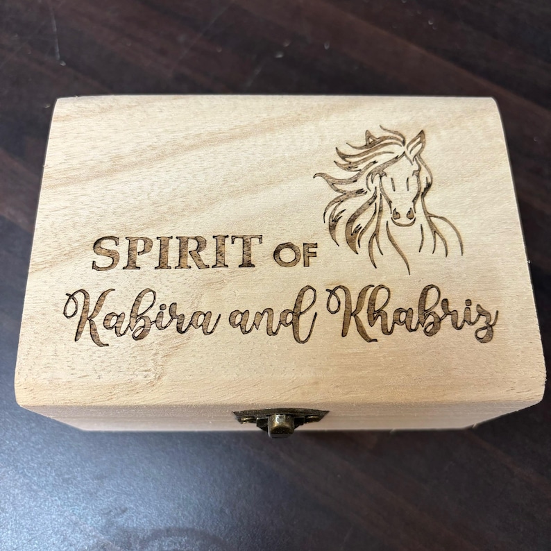 May include: A wooden box with a hinged lid and a brass latch. The box is engraved with the words "SPIRIT OF Kabira and Khabriz" and a horse's head.