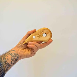 Puede incluir: Una herramienta de madera con forma de lágrima y dos agujeros. La herramienta está etiquetada como "A&B" y "G2".