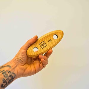 May include: A wooden tool with two holes and the text "02" and "ABS" printed on it. The tool is held in a hand.