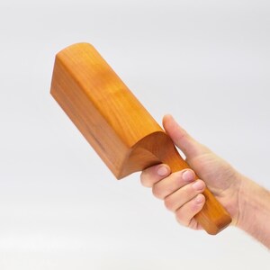 May include: A wooden mallet with a curved handle. The mallet is made of light brown wood and has a smooth finish.