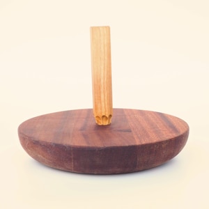 May include: A wooden spinning top with a round base and a tall, cylindrical spindle. The top is made of dark brown wood and the spindle is made of light brown wood.