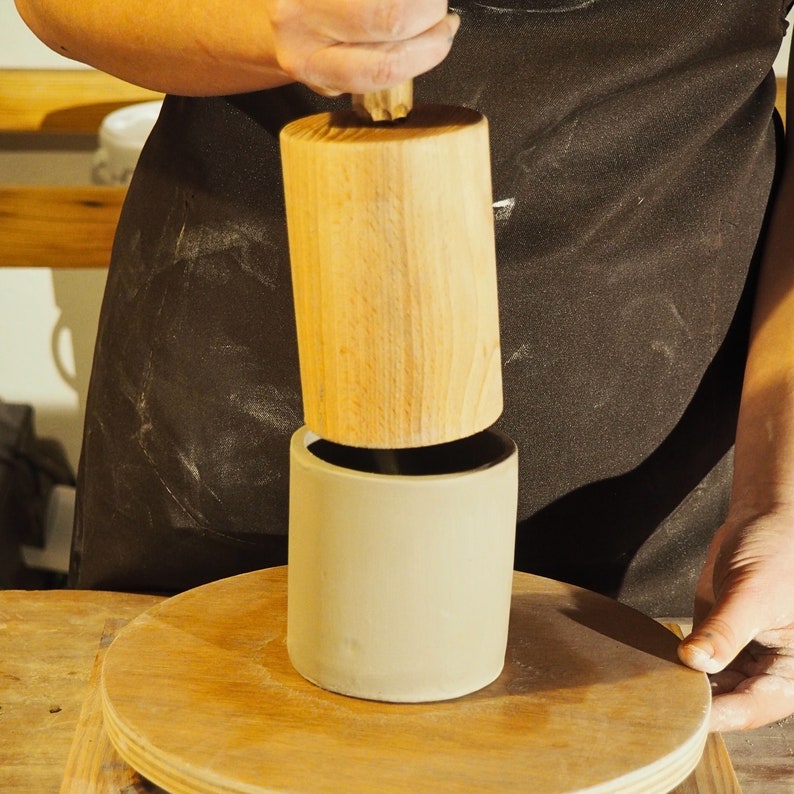 Peut inclure: Un maillet en bois est utilis&eacute; pour presser un mug en c&eacute;ramique beige. Le mug est pos&eacute; sur une surface en bois.