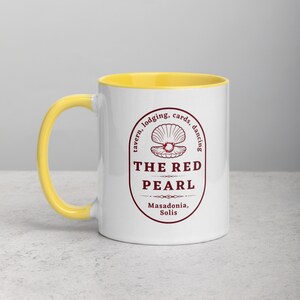 Close-up studio shot of a white ceramic mug with a bright yellow handle and interior. The mug is oriented with the handle facing towards the left. Centered on the mug is a maroon-colored oval logo containing "The Red Pearl" in bold sans-serif letters. Above this title is shell graphic, around logo text include tavern, lodging, cards, dancing, and location "Masadonia, Solis". The image has balanced lighting and is placed against a gradient soft gray background.