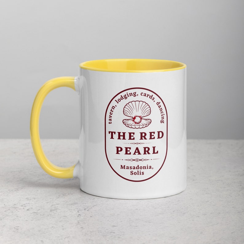 Close-up studio shot of a white ceramic mug with a bright yellow handle and interior. The mug is oriented with the handle facing towards the left. Centered on the mug is a maroon-colored oval logo containing "The Red Pearl" in bold sans-serif letters. Above this title is shell graphic, around logo text include tavern, lodging, cards, dancing, and location "Masadonia, Solis". The image has balanced lighting and is placed against a gradient soft gray background.