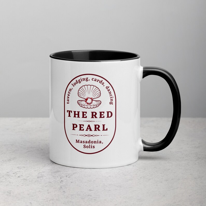 Close-up studio shot of a white ceramic mug with a black handle and interior. The mug is oriented with the handle facing towards the left. Centered on the mug is a maroon-colored oval logo containing "The Red Pearl" in bold sans-serif letters. Above this title is shell graphic, around logo text include tavern, lodging, cards, dancing, and location "Masadonia, Solis". The image has balanced lighting and is placed against a gradient soft gray background.