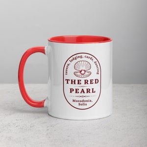Close-up studio shot of a white ceramic mug with a red handle and interior. The mug is oriented with the handle facing towards the left. Centered on the mug is a maroon-colored oval logo containing "The Red Pearl" in bold sans-serif letters. Above this title is shell graphic, around logo text include tavern, lodging, cards, dancing, and location "Masadonia, Solis". The image has balanced lighting and is placed against a gradient soft gray background.