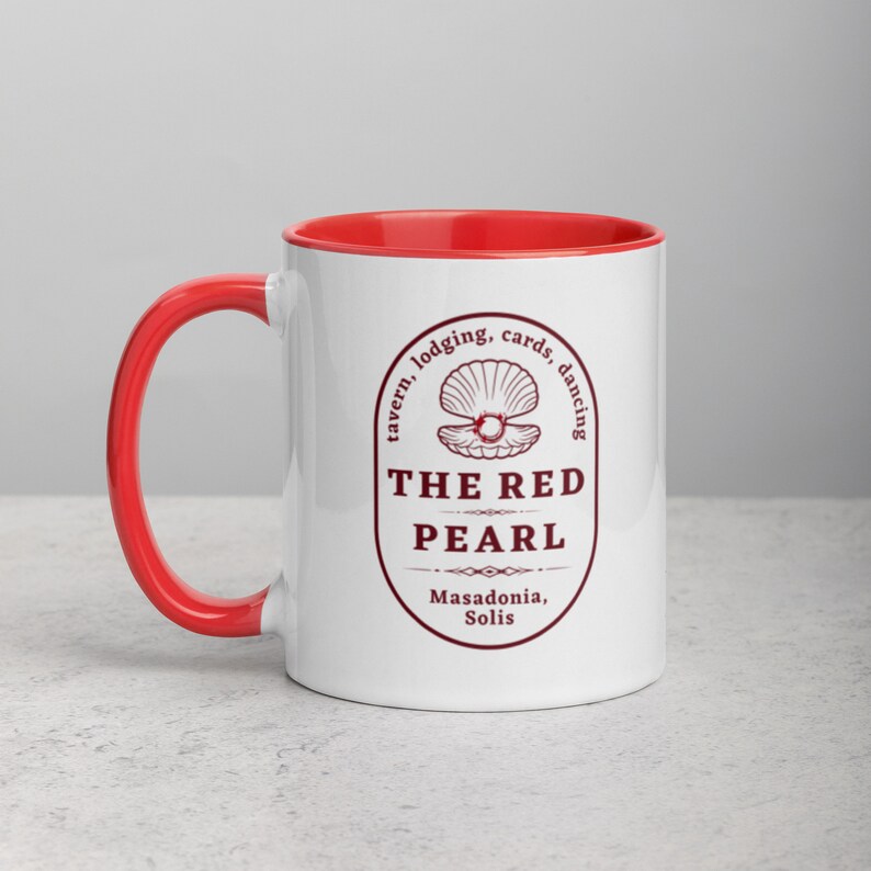 Close-up studio shot of a white ceramic mug with a red handle and interior. The mug is oriented with the handle facing towards the left. Centered on the mug is a maroon-colored oval logo containing "The Red Pearl" in bold sans-serif letters. Above this title is shell graphic, around logo text include tavern, lodging, cards, dancing, and location "Masadonia, Solis". The image has balanced lighting and is placed against a gradient soft gray background.