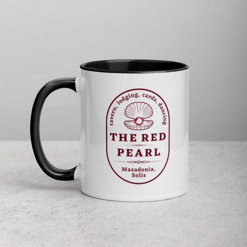 Close-up studio shot of a white ceramic mug with a black handle and interior. The mug is oriented with the handle facing towards the left. Centered on the mug is a maroon-colored oval logo containing "The Red Pearl" in bold sans-serif letters. Above this title is shell graphic, around logo text include tavern, lodging, cards, dancing, and location "Masadonia, Solis". The image has balanced lighting and is placed against a gradient soft gray background.