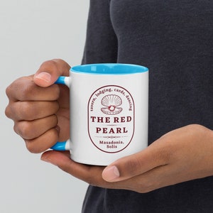 May include: White ceramic mug with a blue rim. The mug features a red logo with the text "The Red Pearl" and a stylized image of a pearl inside a seashell. The logo also includes the text "tavern, lodging, cards, dancing" and "Masadonia, Solis".