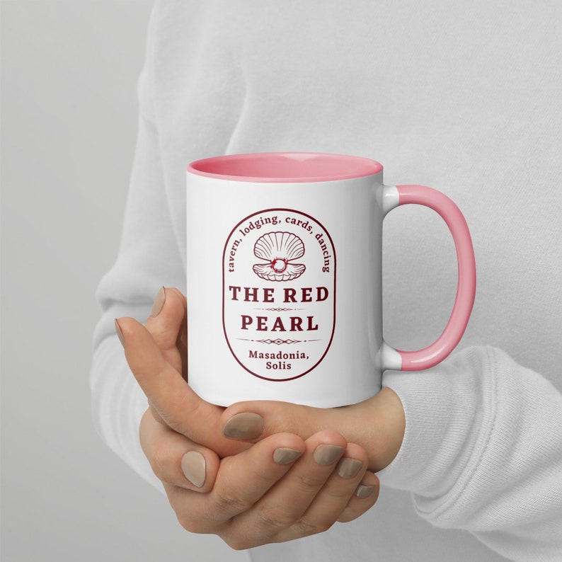 May include: White ceramic mug with a pink rim and handle. The mug features a red graphic of a pearl inside a seashell with the text "The Red Pearl, Masadonia, Solis" and "tavern, lodging, cards, dancing".