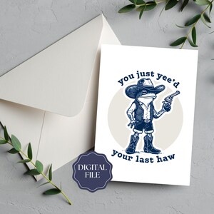 May include: A white greeting card featuring a cartoon frog in cowboy attire, holding a gun. The card displays the text "you just yee'd your last haw." An envelope and a digital file badge are also visible.