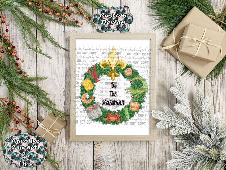 May include: A framed print featuring a green wreath decorated with a gold fleur-de-lis, a crawfish, a shrimp, a crab, and a pot of food. The text in the center reads 'Tis the Seasoning' in black script and block lettering on a white background.