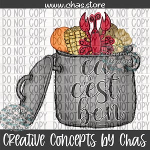May include: A gray pot with a lid open, filled with corn on the cob, a red lobster, and other ingredients. The pot has the text "ca c'est bon" written on it.