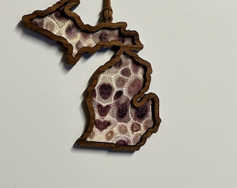 May include: A wooden ornament shaped like the state of Michigan, with a brown leather cord for hanging. The ornament is filled with a white and purple patterned design.