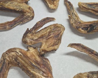 Puede incluir: Varias alitas de pollo deshidratadas, de color marrón claro y bronceado, con una apariencia seca y texturizada. Las alitas están dispersas por el encuadre, mostrando varios ángulos de la piel seca, la estructura ósea y las articulaciones.