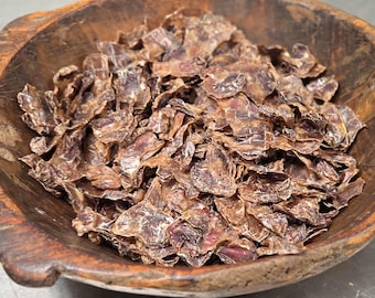 Puede incluir: Un cuenco de madera rústica de color marrón oscuro lleno de una gran cantidad de pequeños trozos de carne seca de color marrón oscuro e irregulares. El cuenco tiene una superficie texturizada y desgastada con vetas e imperfecciones naturales.