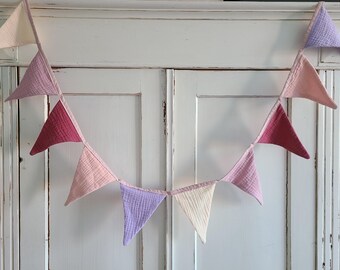 Puede incluir: Una guirnalda de tela de color rosa pastel, morado y crema con banderas triangulares que cuelgan de un armario blanco.