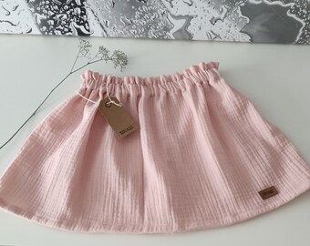 May include: A pale pink, gathered skirt made of a soft, textured fabric. The skirt has a small brown tag with the text "The Wild" on it.