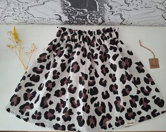 May include: A skirt featuring a white base with a brown and black leopard print pattern. The garment has an elasticated, gathered waistband and a small rectangular fabric label attached to the bottom right corner with the text lulu k.
