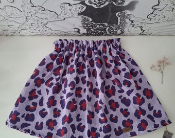 May include: A lilac-colored skirt with a leopard print pattern in dark purple and red. The skirt has a gathered waistband and a flared silhouette. The fabric appears to be lightweight and suitable for warm weather. A small tag is attached to the skirt.